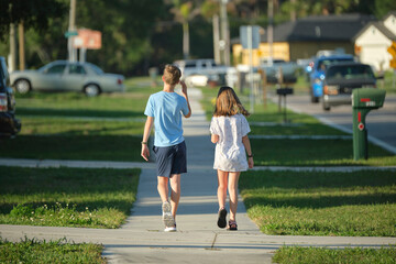 Rear view of two young teenage children, girl and boy, brother and sister walking together on rural street on bright sunny day. Vacation time concept