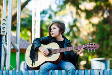 A beautiful little girl, in rock style, sits on stage and plays an acoustic guitar