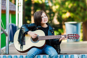 A beautiful little girl, in rock style, sits on stage and plays an acoustic guitar
