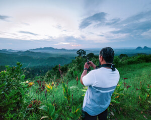 A man is taking video of the mountains during sunrise in Wang Kelian, Perlis, Malaysia.