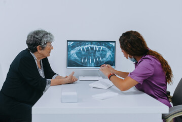 Elderly lady consults with her dentist in a dental office, discussing modern dental prosthetics while examining a computer