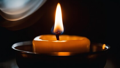 The warm light of a tealight candle casts a soft glow, encapsulated in darkness, emanating a sense of peace and simplicity. - obrazy, fototapety, plakaty