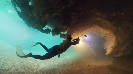 Cave freediving. Freedivers dive inside the cave with underwater camera and explore the intricate seascape of West Papua region, Indonesia