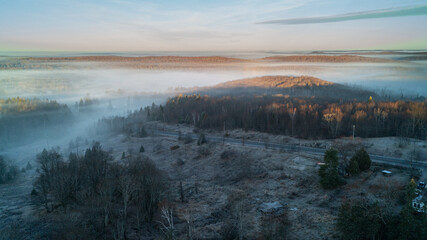 Aerial view of fog over lakes and forests with a road going by at sunrise