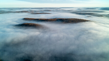 Aerial view above the clouds over forest and lakes at sunrise
