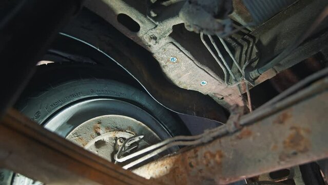 Undercarriage perspective highlighting a tire and suspension system, detailing the wear and workmanship in a car service setting.