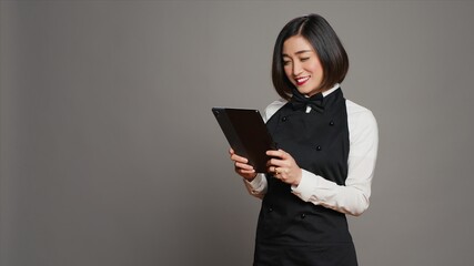 Asian restaurant server checking all table reservations on tablet, browsing through clients...