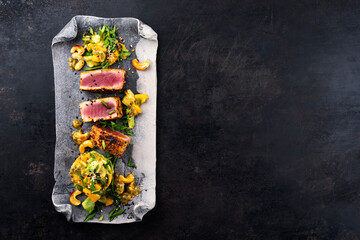 Traditional Japanese gourmet tuna fish steak tataki with tropical fruit tartar and cashew nuts served as top view on a Nordic design tray with copy space right - obrazy, fototapety, plakaty