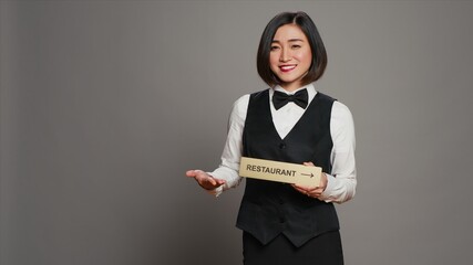 Asian hotel concierge holding restaurant sign to indicate direction, pointing towards dining area....