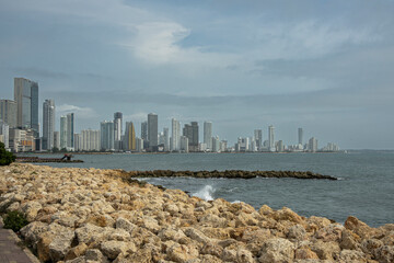 Naklejka premium Cartagena, Colombia - July 25, 2023: Seen from where Calle 33 meets Avenida Santander, breakwater and Tall buildings skyline on NW side of Bocagrande peninsula. Rocky shore upfront