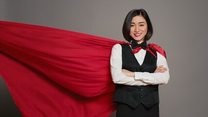 Asian receptionist posing with red superhero cape on camera, feeling confident and powerful while...