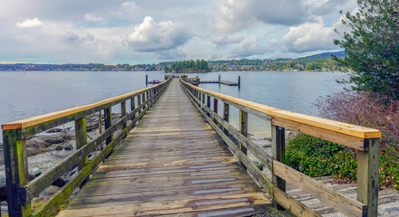 Wooden pier at Belcarra public beach park, BC, on a cloudy pre-Spring day, with the town of Deep Cove visible on horizon.