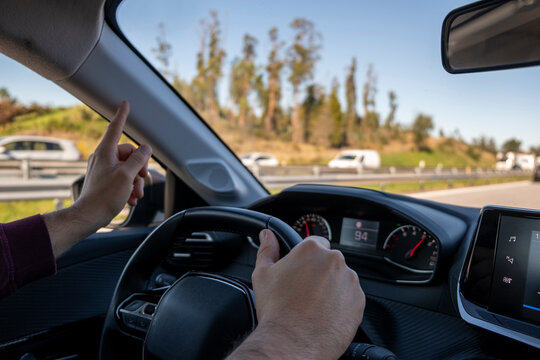Drivers hand on car steering wheel and pointing at traffic on the highway in the opposite direction. Driver POV to blurred road with traffic in the background.