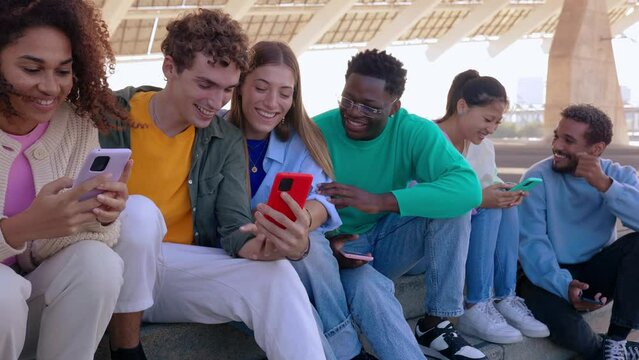 Young group of multiracial friends having fun using mobile phone device sitting together outdoors. Millennial people enjoying social media content on cellphone app. Youth concept.