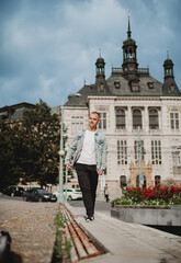 Obraz premium A man in a white shirt and black pants walks down a sidewalk in front of a large building
