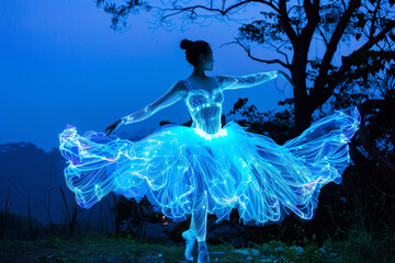 Ballerina in neon glowing fluffy dress. Romantic outdoors scene at dusk, girl dancing on tips of feet in pointe shoes and theatrical costume. Copy space