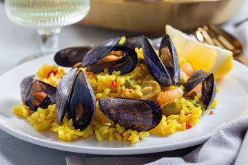 Paella with mussels and shrimps, on white plate, with lemon and white wine, horizontal