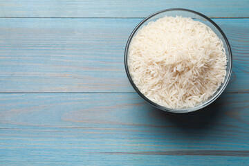 Raw basmati rice in bowl on light blue wooden table, top view. Space for text