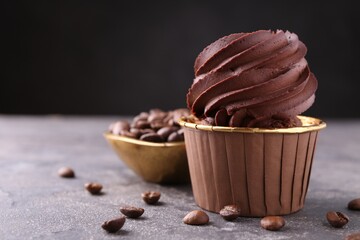 Delicious chocolate cupcake and coffee beans on grey textured table, closeup. Space for text
