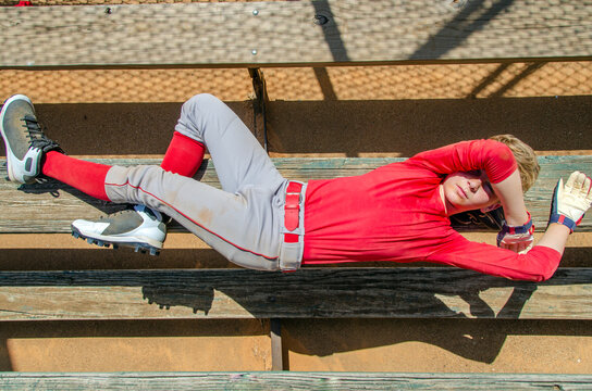 Youth preteen boy baseball player lying down on dugout bench exhausted and dirty after a game - Powered by Adobe