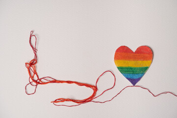 corazón pintado con arcoíris y unido a un hilo rojo