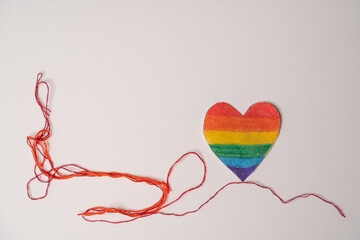 corazón de tela arcoíris con fondo blanco e hilo rojo desenredado hacia un costado