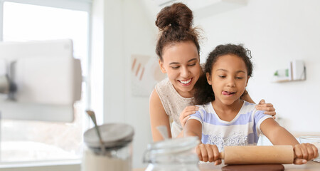 African-American little girl and her mother rolling out dough in kitchen