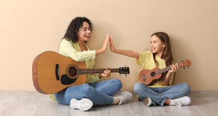 Young woman and girl with acoustic guitars giving each other high-five on beige background