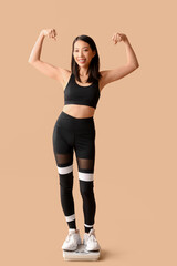 Beautiful young Asian woman with scales showing muscles on beige background. Weight loss concept