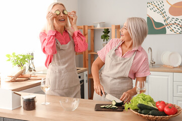 Mature female friends cutting cucumber in kitchen