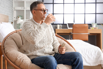 Middle-aged man with glass of water taking pills at home