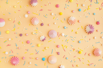 Sweet colorful sprinkles with meringues scattered on beige background