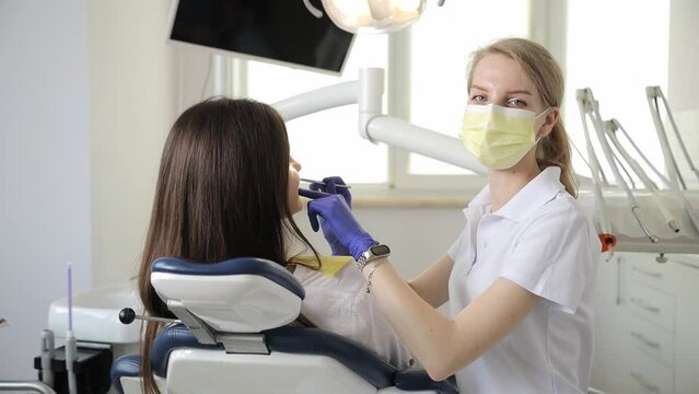 A female dentist treats the teeth of a young brunette female patient in a modern dental office. 