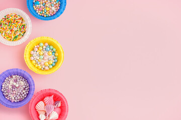 Paper bowls with colorful sweet sprinkles and meringue on pink background