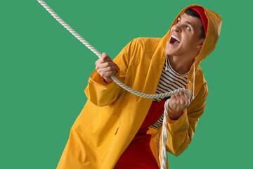 Young sailor in raincoat pulling rope on green background