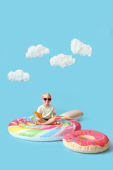 Cute little boy with sunscreen cream sitting on swim mattress against blue background