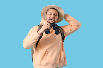 Male tourist with backpack and binoculars on blue background