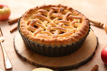 Wooden tray with tasty homemade apple pie, fruits and cinnamon on beige grunge background, closeup