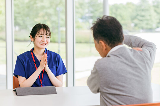 高齢男性患者のリハビリ結果を笑顔で聞く理学療法士・看護師・介護士の女性（励ます・応援・喜ぶ）
