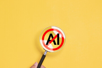 Hand holding magnifying glass focus to No AI symbol on yellow background for Stop AI..