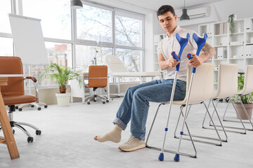 Injured young man after accident with crutches sitting in clinic