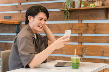Fototapeta na wymiar カフェでスマホとパソコンを使う若いアジア人男性（驚く・投資・失敗・トラブル・ショック） 