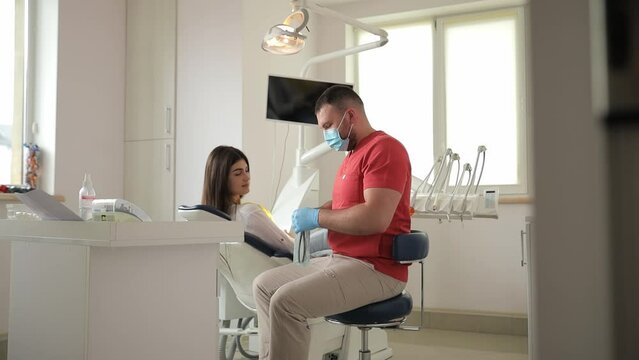 A Dentist In A Medical Mask Discusses A Treatment Plan With A Patient.