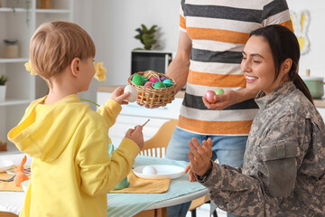Female soldier with her little son painting Easter eggs in kitchen