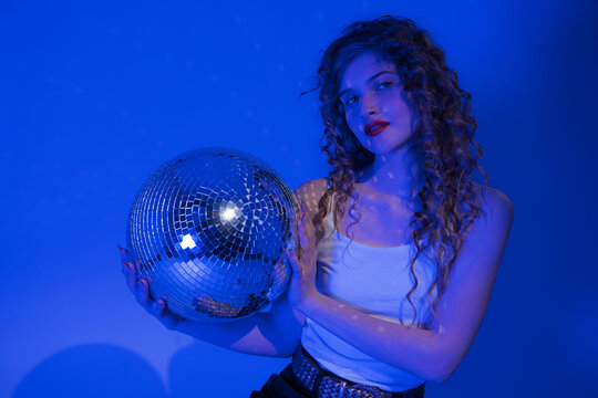 Woman looks absolutely stunning as she poses with disco ball in nightclub. Blue neon lights add touch of sensuality to scene, making it even more exciting. Woman knows how to party and have good time