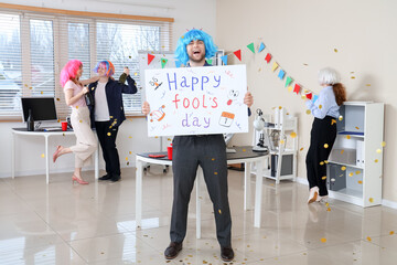 Business man in funny wig with poster celebrating April Fools' Day at office party