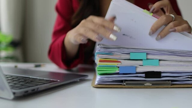 A woman doing paperwork is searching for a sheet of paper in a pile of documents on her desk.