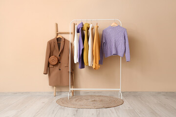 Rack of stylish clothes and rug near beige wall