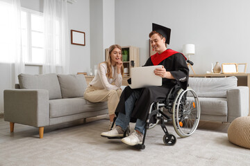 Male graduate in wheelchair with laptop and friend at home
