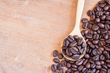 Coffee beans in wooden spoon on wooden table background